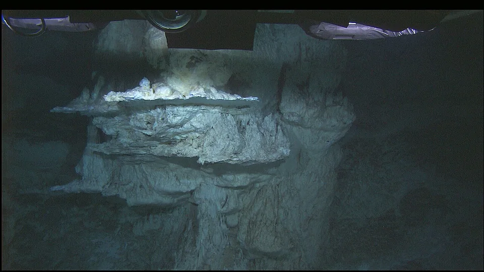 Pale mineral terraces at the Lost City hydrothermal field are illuminated against the dark deep sea.