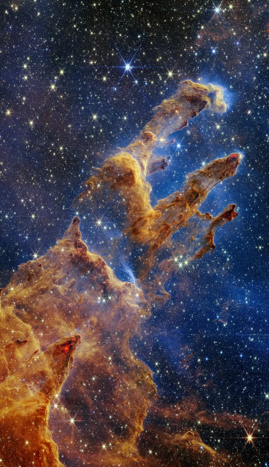Gold and rusty brown pillars of gas and dust rise diagonally through a deep blue field filled with stars.