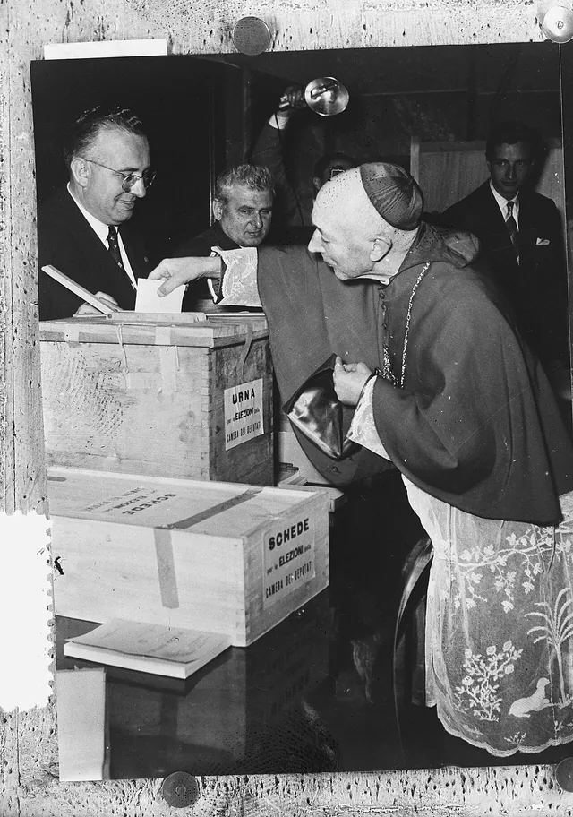 Ildefonso Schuster in clerical dress casting a ballot, surrounded by officials.