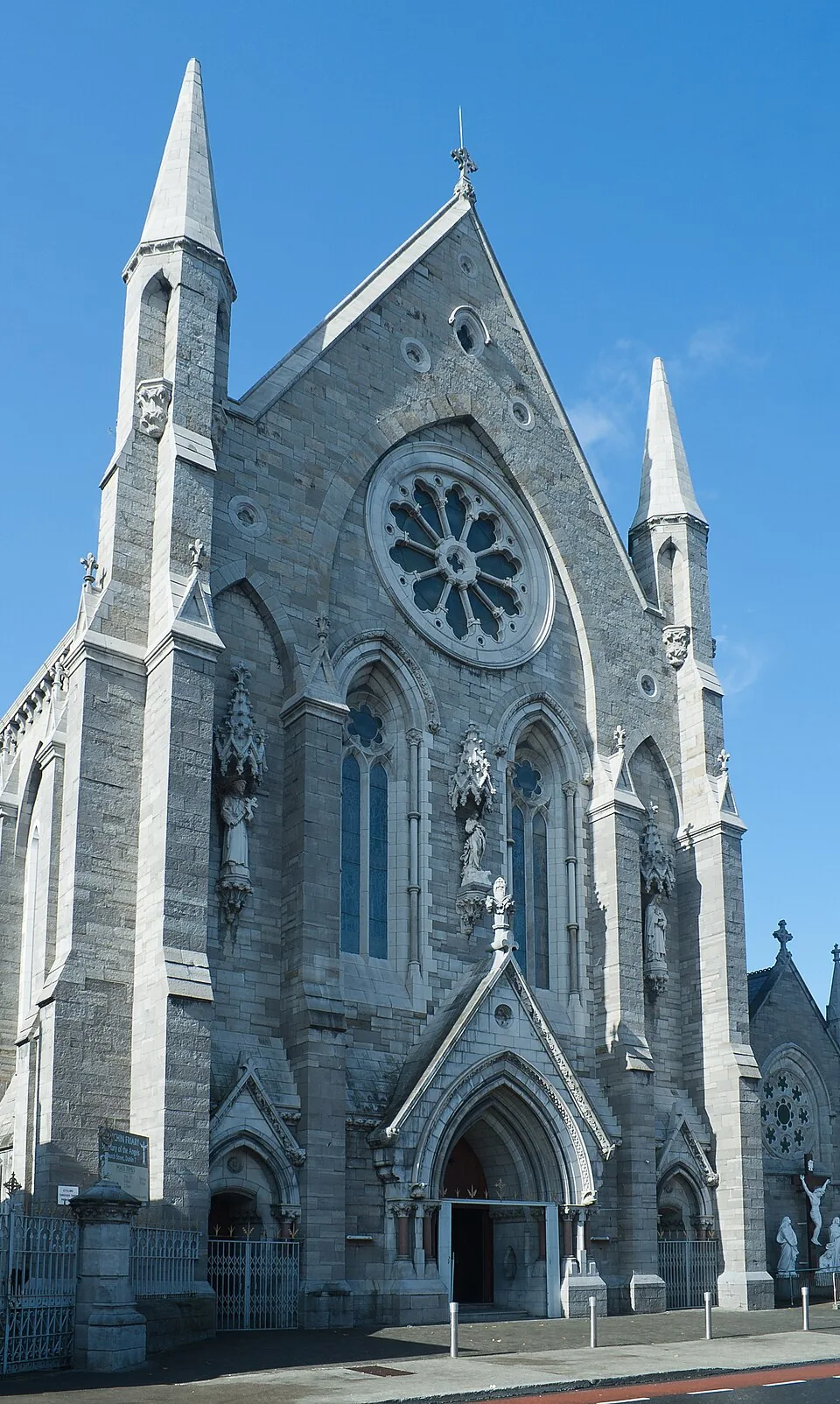 The stone facade and towers of St Mary of the Angels church in Dublin under a blue sky.